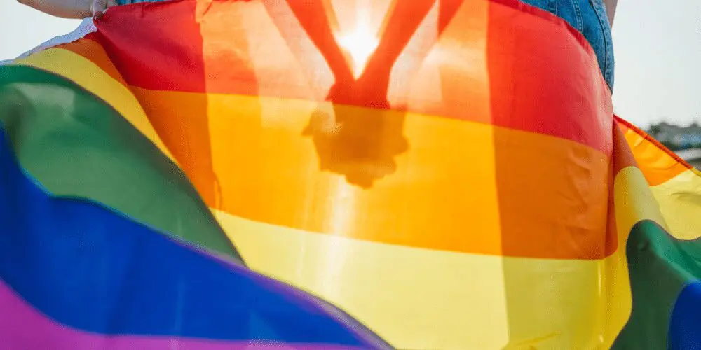 Hands holding behind pride flag.