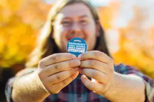 person holding democracy now sticker