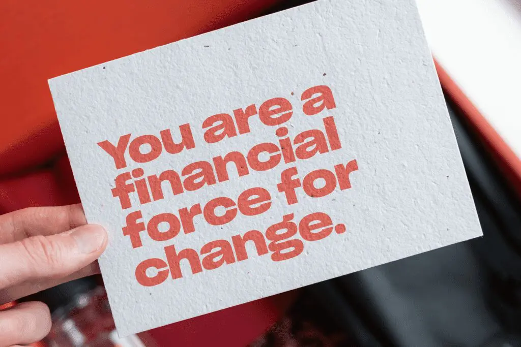 A person’s hand holding up a seed paper post card that reads “You are a financial force for change.”