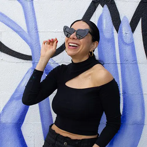 Alma standing in front of a mural with sunglasses on
