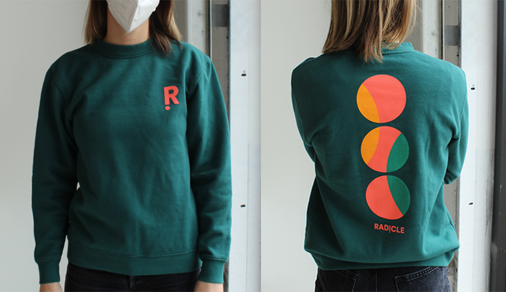 Front and back view of a woman wearing a teal Rad!cle branded crewneck sweater. 