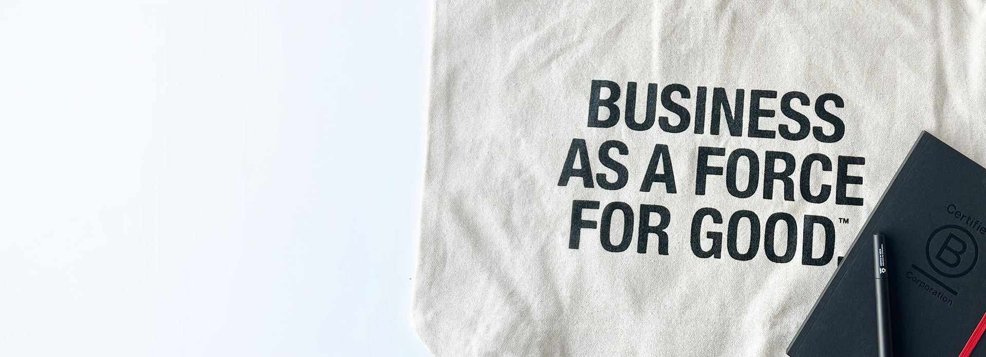 business as a force for good printed on a canvas tote bag with a black BCorp branded notebook and pen.