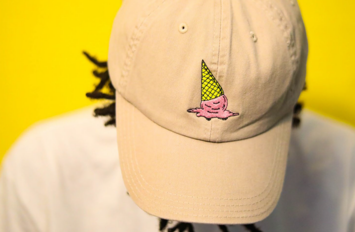 person wearing a cream ball cap with an embroidery imprint depicting an upside down icecream cone.