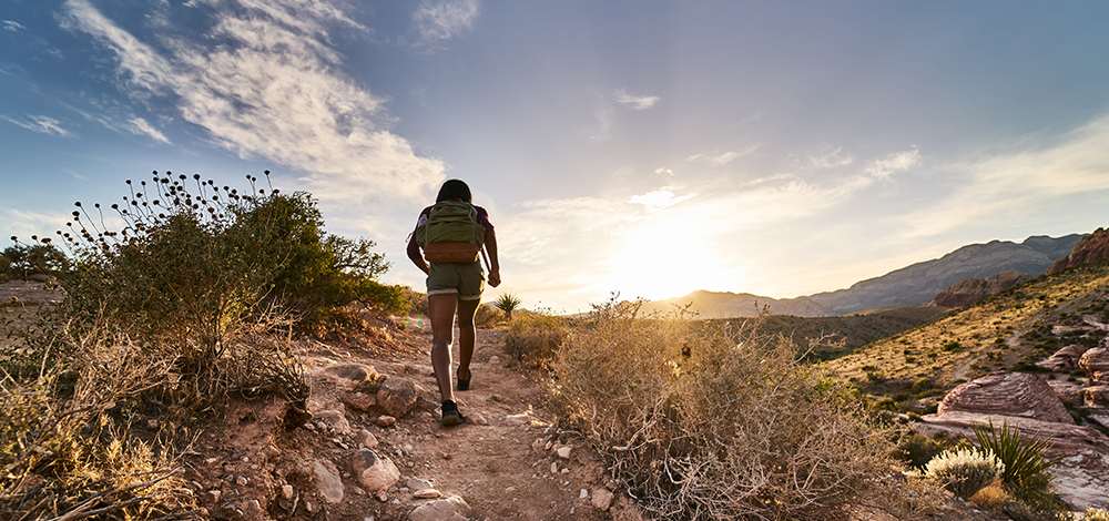 Woman hiking on trail in front of mountains and sunset.