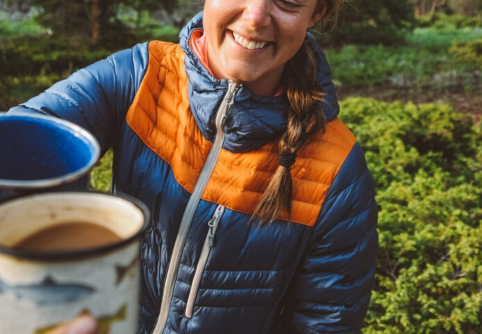 person in custom puffy jacket camping and cheersing coffee cups
