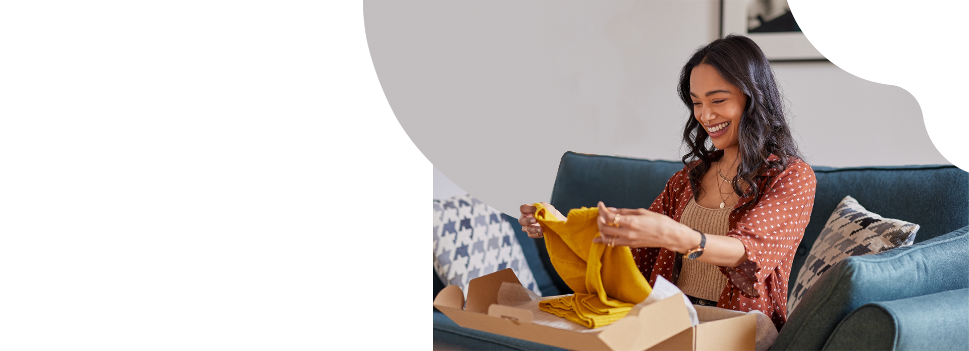 woman sitting on couch opening package and holding a yellow sweater