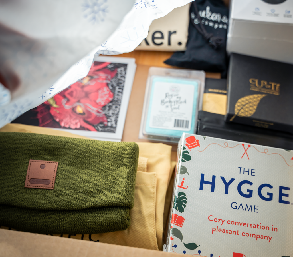 A piece of custom tissue is being lifted off of Employee Gifts inside a box with branded Thinkific beanie and the game Hygge and several other items blurred in the background