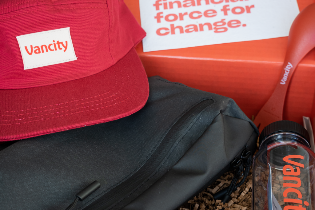 A red box with Vancity branded items, focusing on a red Vancity baseball cap, Miir crossbody bag, and a Fill It Forward Reusable water bottle.