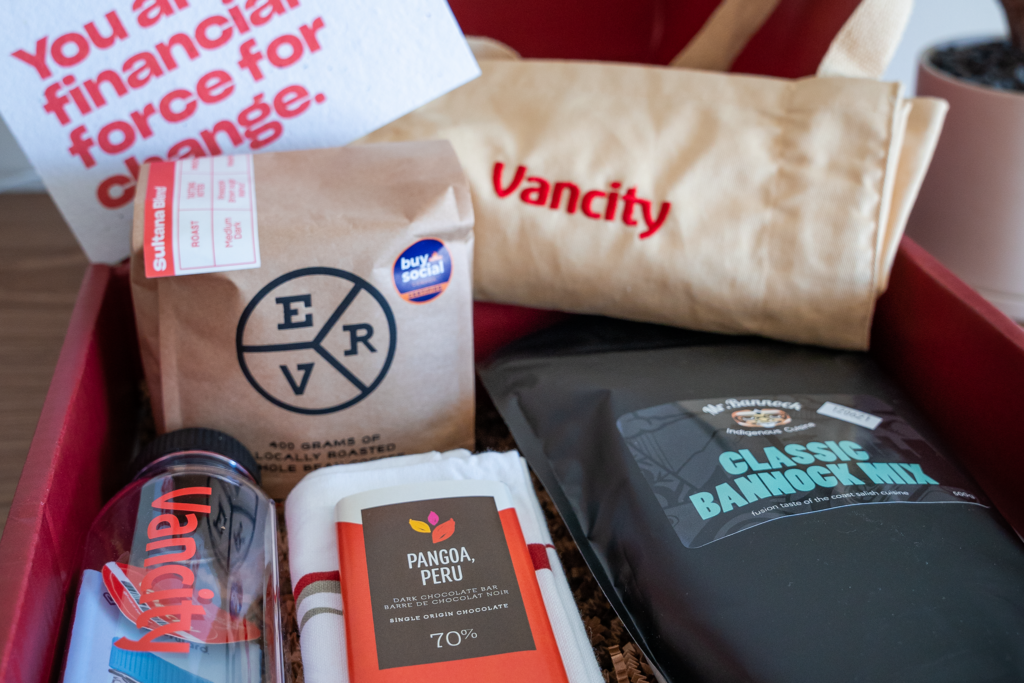 A red box filled with Vancity branded items. Including a water bottle, East Van Roasters coffee, an apron, Mr.Bannock bannock mix and ethically sourced fair trade chocolate. 