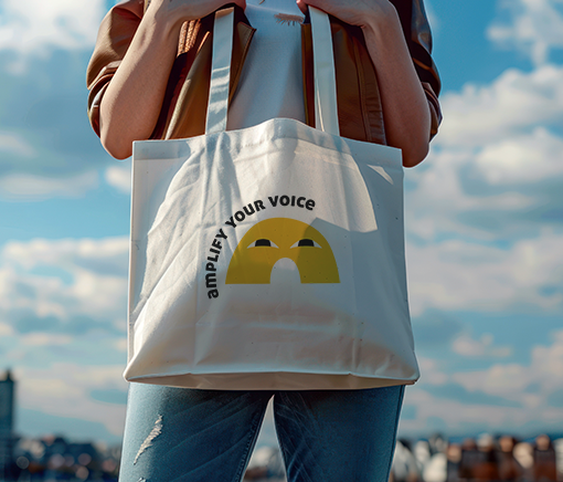 person holding a cotton totebag with graphic that reads amplify your voice and clouds in the background