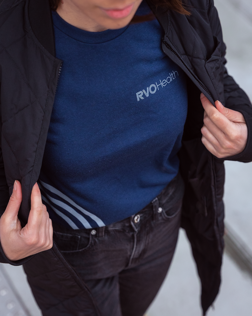 Person showing off their t-shirt through their open black jacket. The t-shirt reads RVO Health.