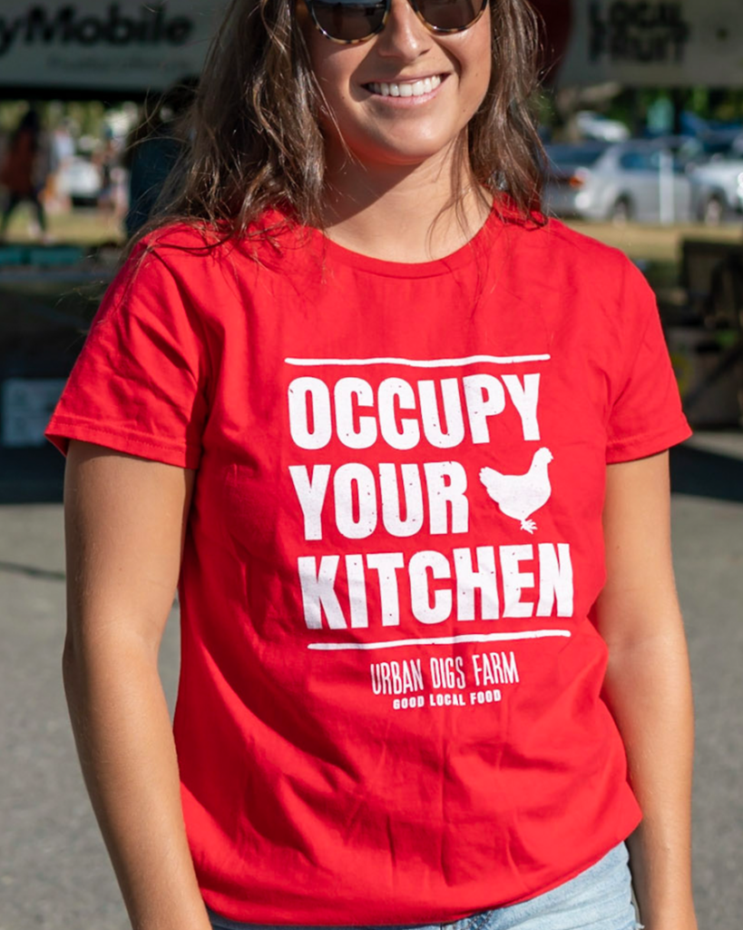 woman wearing a read t-shirt that reads OCCUPY YOUR KITCHEN with the an image of a chicken. 