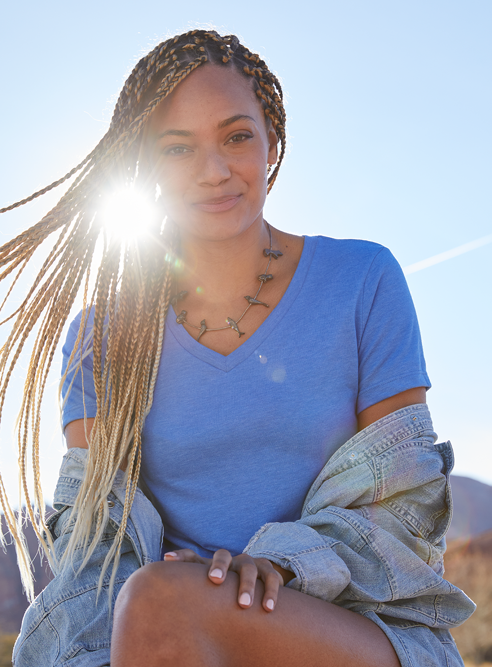 woman wearing a blue v neck tshirt with the sun coming from behind her.