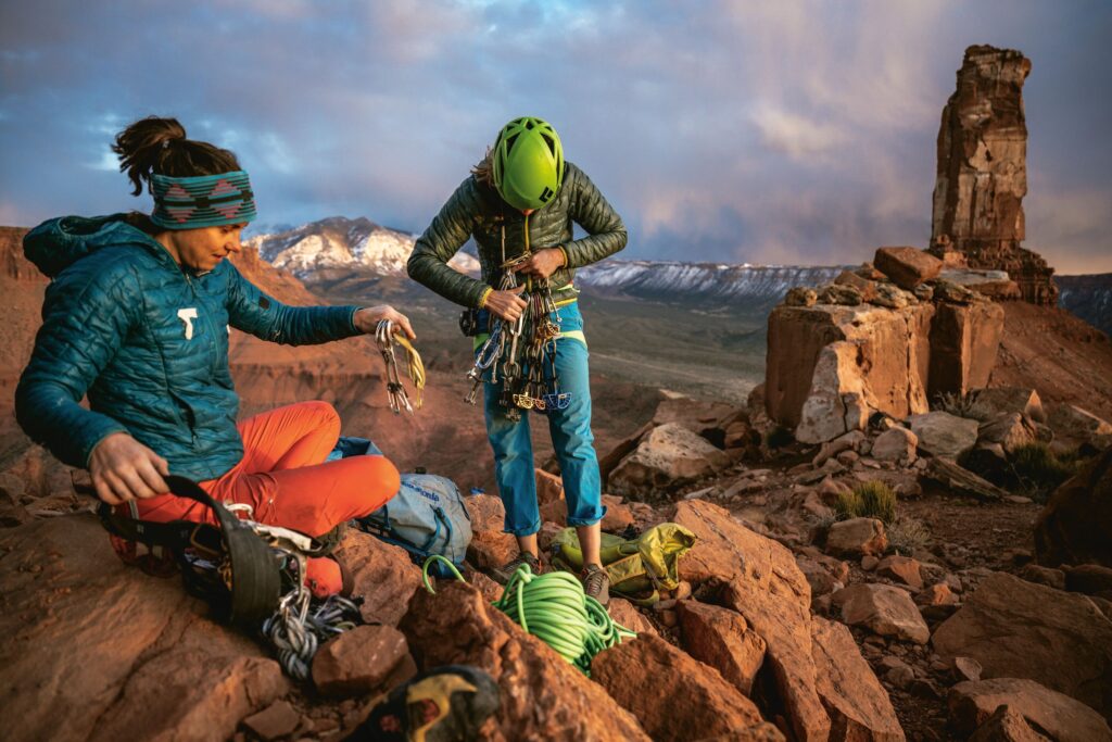 image of women wearing patagonia gear about to go climbing - there are rocks and a mountain range surrounding them.