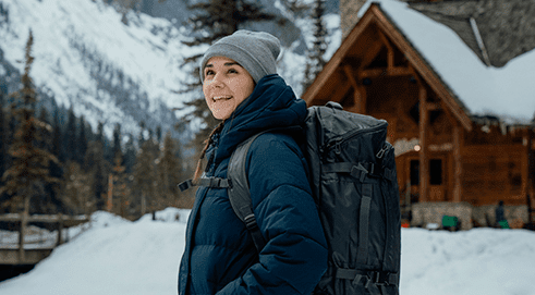 woman wearing brandable Stormtech gear in front of a chalet on a mountain in winter