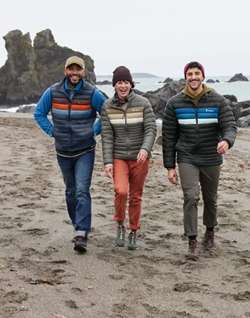 Three people walking up the beach wearing cotopaxi jackets