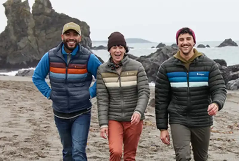 Three people walking up the beach wearing cotopaxi jackets